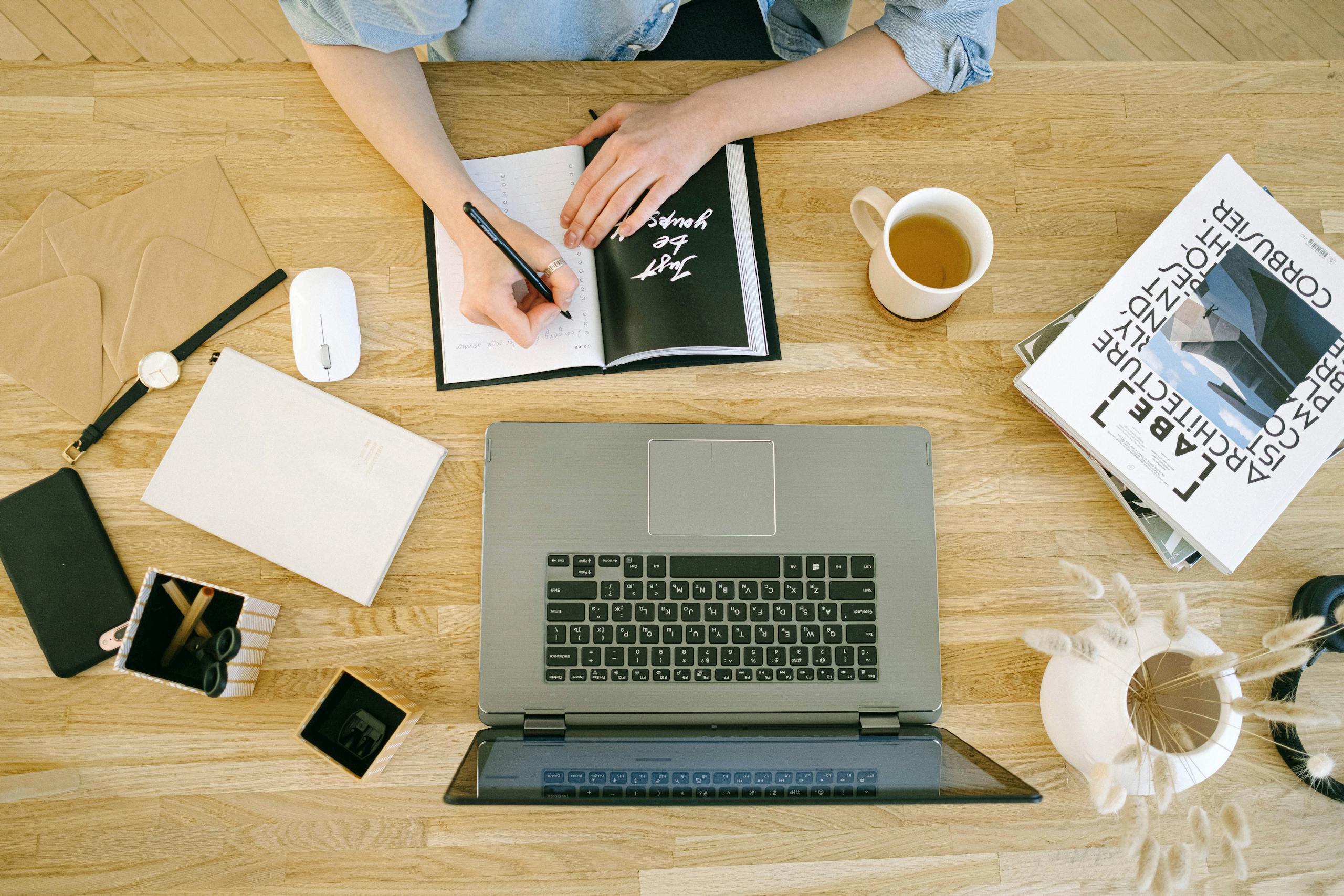 JuicyCRM JuicyCRM for Virtual Assistants | A woman writing notes at a home office desk with a laptop and coffee cup.