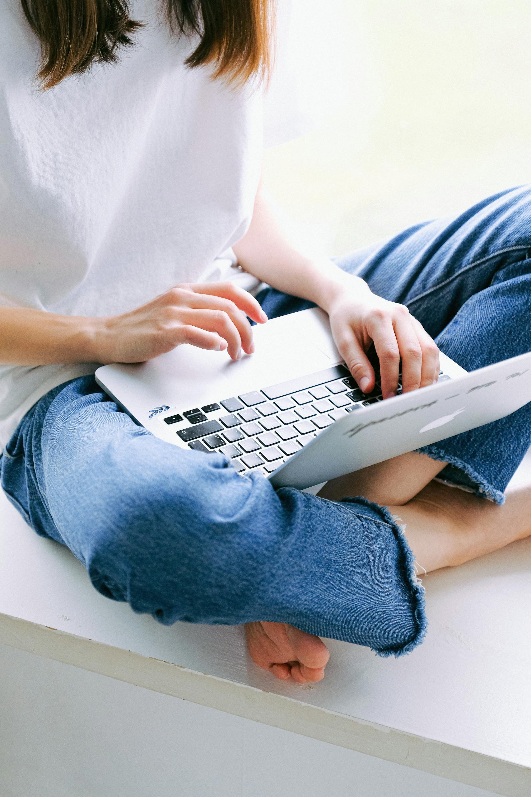 Woman sitting cross-legged in casual jeans working on a laptop indoors | JuicyCRM for Subscription Businesses